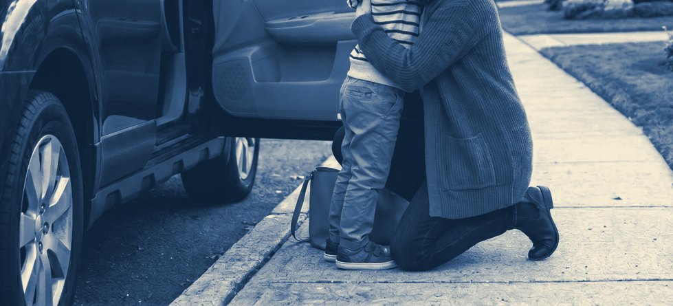 A parent kneels beside a young child at the curb next to the family car.